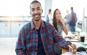 Smiling employee at desk with colleagues behind, representing Microsoft Configuring Windows 10 Online Course.