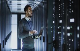 A man works on a laptop in a server room, representing the Microsoft Networking with Windows Server 2016 Online course.