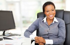 Professional businesswoman smiling at her desk, promoting Microsoft Office & Payroll course in a positive workspace.