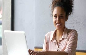 Smiling woman sitting in front of a laptop, representing the Microsoft Outlook 2010 course and showcasing a positive, engaged work environment.