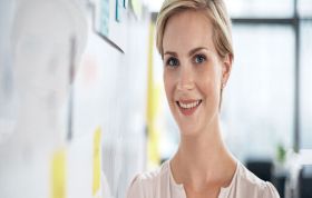 Cheerful woman standing in front of whiteboard, showcasing ideas, representing the Microsoft PowerPoint 2010 Course for presentation skills.