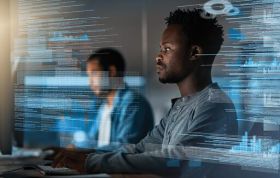 Two men collaborate in front of a large screen, working on computers, representing the MTA Security Fundamentals Online course