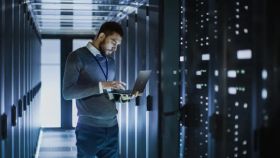 Man holds laptop in server room, surrounded by servers, representing MTA Windows Server Administration Fundamentals Online course.