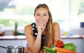 Smiling woman at table with fresh vegetables, representing the Online Nutrition Course focused on healthy eating and lifestyle habits.