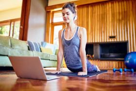 Woman sitting on the floor in a cozy space, focused on laptop, representing the Online Yoga Training course for flexibility and mindfulness.