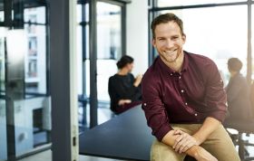 A man smiles at his desk in a bright office, representing the Oracle and Microsoft Database Training course.