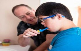 A man and young boy brushing teeth together in bathroom, promoting Oral Care for people with Additional Needs in a supportive setting.