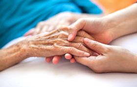 Young woman’s hand gently holding elderly hands, representing Palliative and End of Life care for those with life-limiting illness.