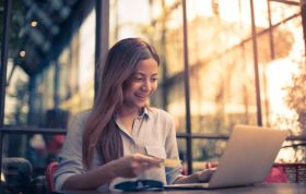 Smiling girl holding a paper while looking at her laptop, representing Pay and Reward and what the law states regarding payslips.