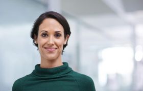 A cheerful woman in an office smiles while working, representing the PC Hacking and Forensic Investigator course.
