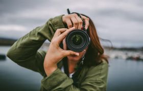 Woman taking a photo outdoors with a camera, focused and engaged, representing the Photography Online Course for creative skills.