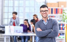 Man wearing glasses stands confidently before diverse group, representing the PRINCE2 Foundation Online Course for project management basics.
