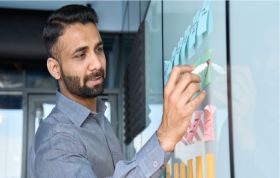 Man writing on a sticky note on a board, demonstrating skills from the Project Management Professional (PMP) Online course.