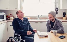 Disabled man in wheelchair talking with young man at tea table, highlighting Protection of Adults and Safeguarding from Abuse.