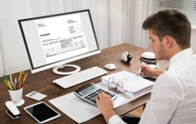 Man working with files at desk in front of monitor, learning QuickBooks to confidently support various types of clients.