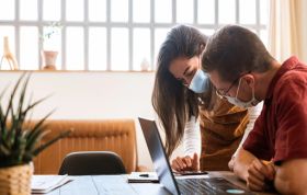 Two masked individuals collaborate on a laptop in a shared workspace, representing the Return to Work COVID-19 Guide course.