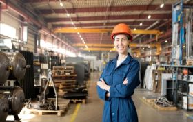 Smiling female employee standing in factory, highlighting Risk Assessment and identifying major risks in the workplace.