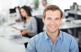 Smiling man standing in front of computer screen, representing the SharePoint Core Solutions 2013 Exam 70-331 course for collaboration skills.