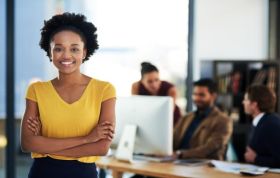 Cheerful young woman in front of colleagues, representing the Six Sigma Black Belt Online Course for leadership and quality management skills.