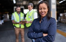 Woman standing in front of warehouse with coworkers, representing the Six Sigma Green Belt Online Course for process improvement skills.