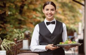 A woman in a black apron holds a tray with a fresh salad, representing the Table Service and Hosting Collection Online Course.