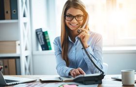 Smiling woman with glasses on phone call, representing the Complete Microsoft Excel Course in a professional setting.