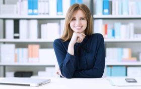 Smiling woman at desk with bookshelf behind her, representing the Unconscious Bias Online course with focus on inclusivity and awareness.