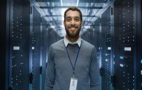 Smiling man in a server room with networking equipment, representing the VMware vSphere 6.7 Fundamentals Online Course.