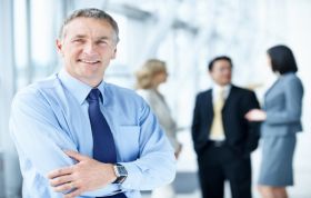 Man standing with arms crossed, others talking behind him, representing Windows Server Network Infrastructure Online Course.