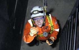 Man in orange jacket and safety gear descending ladder, representing the Working in Confined Spaces Online Course with safety best practices.